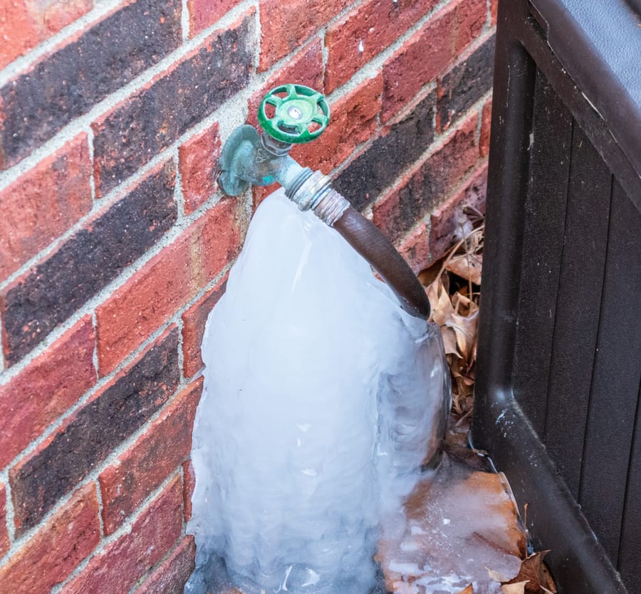 Frozen outdoor hose bib connected to a brick exterior wall during cold weather.