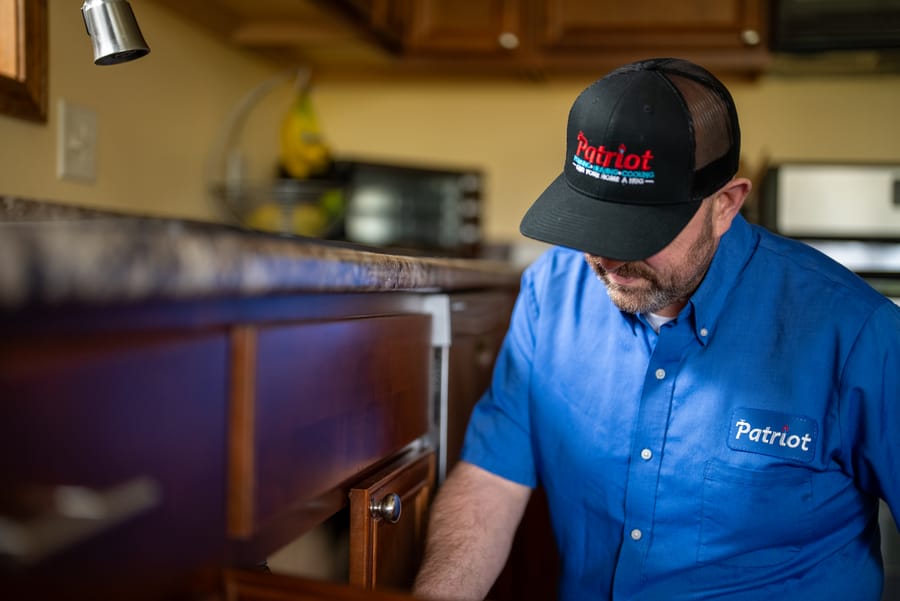 Patriot Plumbing technician inspecting kitchen plumbing beneath a sink in a Wenatchee home.